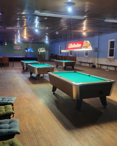 A spacious room with several pool tables, illuminated by colorful lights and a Budweiser sign.
