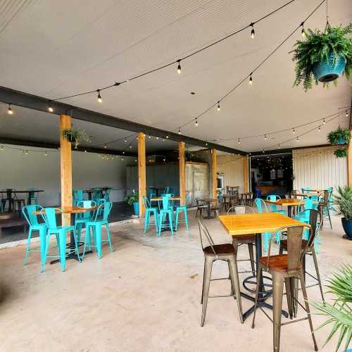 A spacious outdoor dining area with turquoise tables and chairs, string lights, and potted plants.