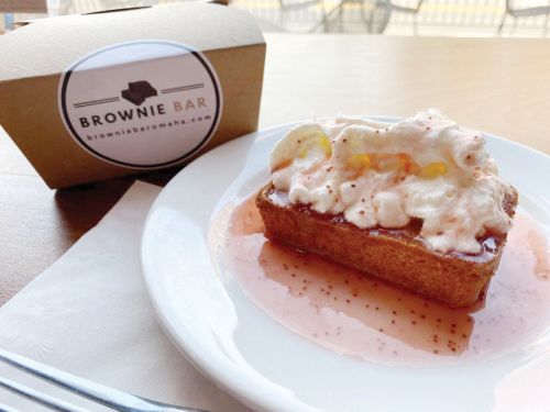 A dessert with whipped cream and fruit on a plate, next to a box labeled "Brownie Bar."