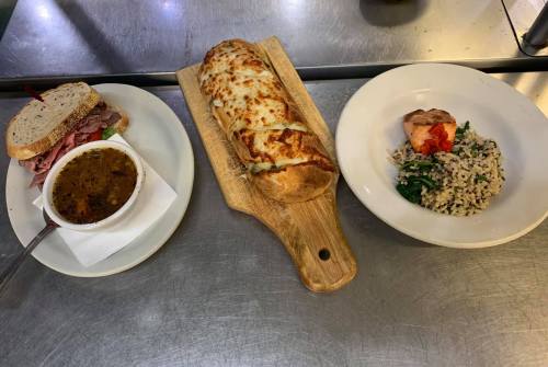 A plate with a sandwich, a bowl of soup, a cheesy bread loaf, and a dish of rice with vegetables and salmon.