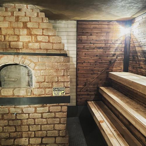 Interior of a sauna featuring a stone heater, wooden benches, and caution signs on the wall. Warm, inviting atmosphere.