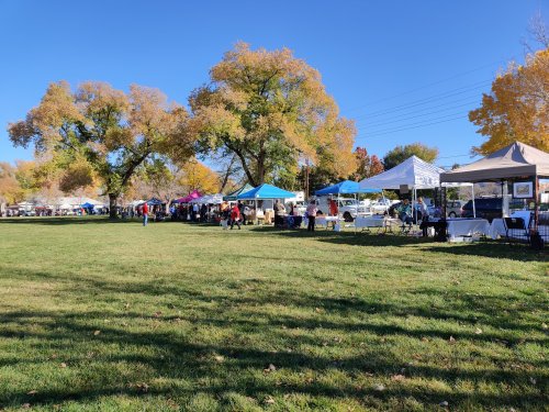A vibrant outdoor market with colorful tents and trees in autumn foliage under a clear blue sky.
