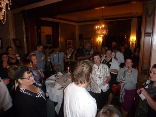 A crowded room filled with people socializing at a formal event, with tables set for dining and elegant decor.