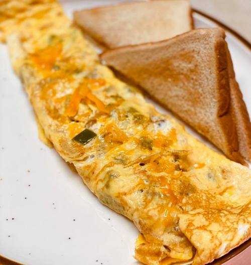 A fluffy omelette with cheese and vegetables, served with two slices of toasted bread on a white plate.