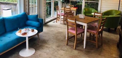 A cozy café interior featuring a blue couch, small tables, and chairs, with pastries on a white table.