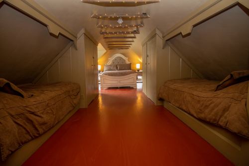 Cozy attic room with two beds, warm lighting, and a central queen bed, featuring sloped ceilings and wooden floors.