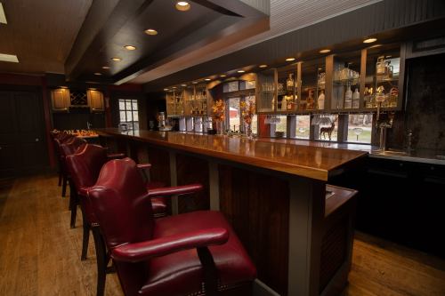 A stylish bar with wooden countertops, red leather stools, and shelves lined with various glassware and bottles.