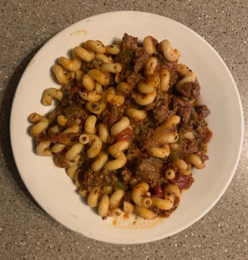 A plate of pasta with ground meat and tomato sauce, garnished with herbs, on a gray countertop.