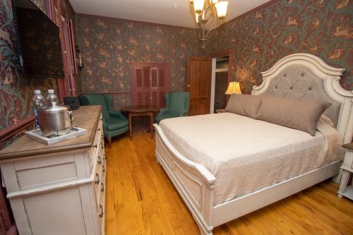 Cozy bedroom with a large bed, vintage decor, green chairs, and a wooden dresser in a warmly lit setting.
