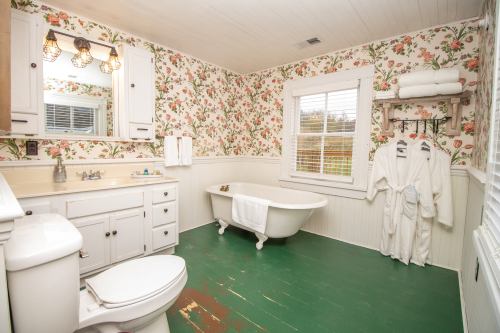 Bright bathroom with floral wallpaper, a clawfoot tub, green floor, and white towels hanging on a rack.