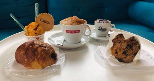 A table with a cup of coffee, gelato, a croissant, and two cookies on plates, all set against a blue background.