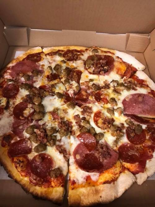 A pizza in a box topped with pepperoni, sausage, and melted cheese, with several slices cut.