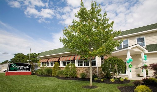 Exterior view of Fitzpatrick's Deli & Steakhouse, featuring a green sign, landscaping, and a cloudy sky.