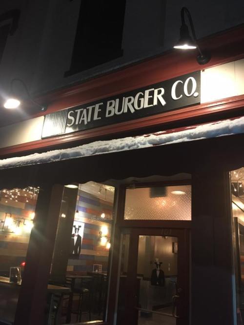Sign for "State Burger Co." illuminated at night, with a cozy restaurant entrance visible below.
