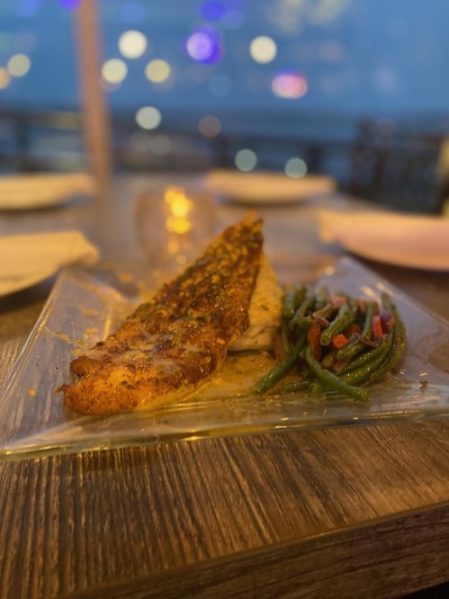 A plate of grilled fish with a crust, served alongside sautéed green beans, set in a softly lit restaurant.