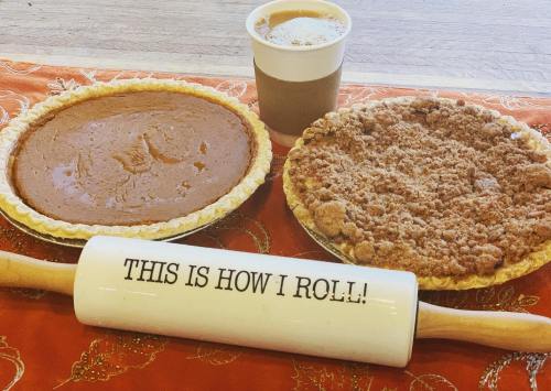 Two pies on a table, one pumpkin and one crumb, with a coffee cup and a rolling pin that says "THIS IS HOW I ROLL!"