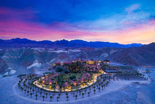 Aerial view of a resort surrounded by mountains at sunset, with palm trees and colorful sky.