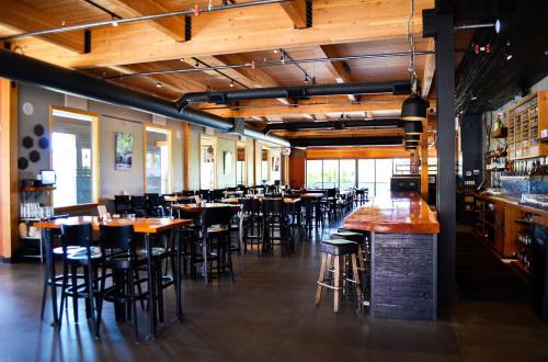 A spacious restaurant interior with wooden beams, tables, and a bar area, featuring large windows and modern decor.
