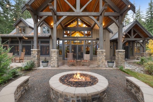 A cozy outdoor seating area with a fire pit, surrounded by a modern wooden cabin and lush trees.