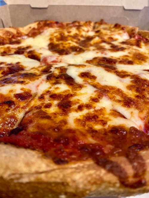 Close-up of a cheesy pizza with a golden crust, showing melted cheese and tomato sauce in a takeout box.