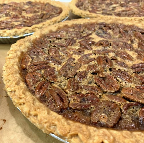 Three pecan pies with a golden crust and a rich, nutty filling, showcasing a glossy layer of pecans on top.