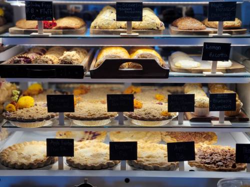 A display case filled with various baked goods, including pies and pastries, each labeled with small black signs.