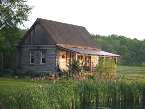 A rustic log cabin surrounded by lush greenery and a pond, with soft morning light illuminating its facade.