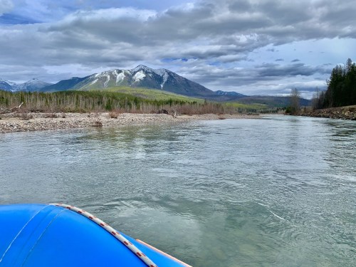A view of a calm river with mountains in the background under a cloudy sky, seen from a blue boat.