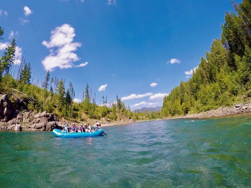 A group of people rafting on a river surrounded by lush green trees and a clear blue sky.