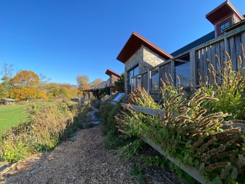 A stone building with a wooden fence, surrounded by greenery and autumn trees under a clear blue sky.