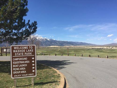 Sign welcoming visitors to Washoe Lake State Park, with a scenic view of mountains and open fields in the background.