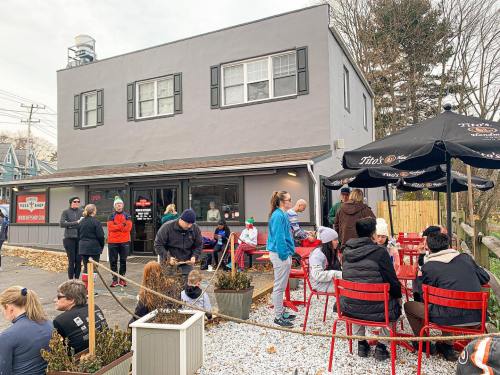 A busy restaurant exterior with people dining outside and a line forming at the entrance on a cool day.