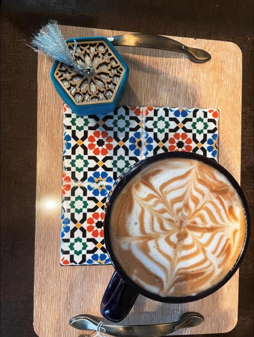 A beautifully crafted coffee with latte art on a decorative tile, accompanied by a small ornate container.