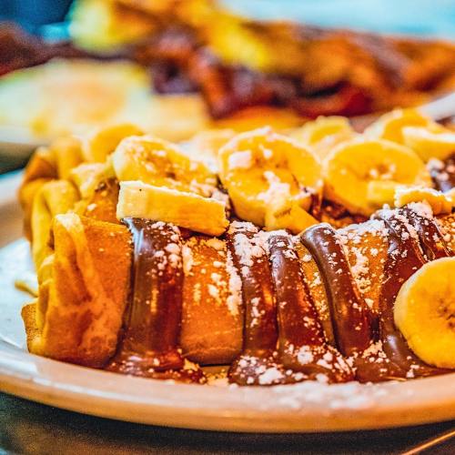 A plate of crepes topped with banana slices, chocolate sauce, and powdered sugar.