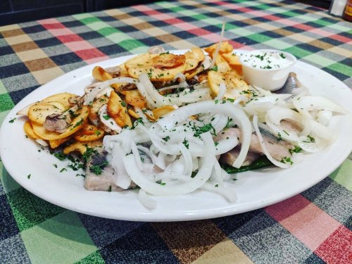 A plate of sliced fish topped with onions, served with crispy potato slices and a small bowl of sauce.