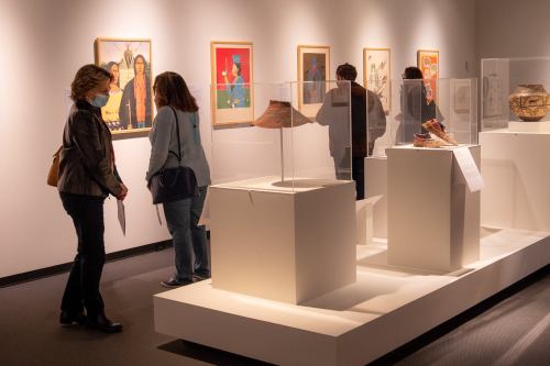 Visitors explore an art exhibit featuring framed artworks and displayed artifacts in a gallery setting.