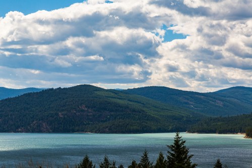 A serene lake surrounded by green mountains under a partly cloudy sky.