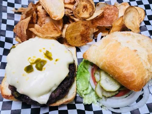 A juicy burger with melted cheese and toppings, served with a side of crispy potato chips on a checkered paper.