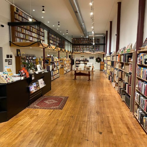 A cozy bookstore interior with wooden floors, tall bookshelves, and a central display table. Warm lighting enhances the atmosphere.