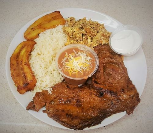 A plate of grilled steak, rice, fried plantains, scrambled eggs, beans, and a side of sour cream.