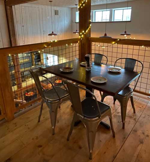 A cozy restaurant interior with a wooden balcony, a table set for dining, and string lights creating a warm ambiance.