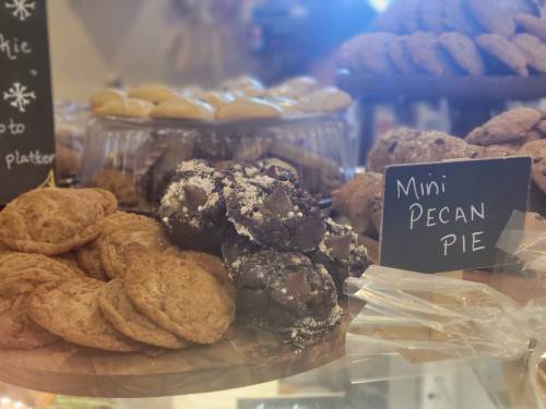 A display of assorted baked goods, including cookies and mini pecan pies, with a chalkboard label.