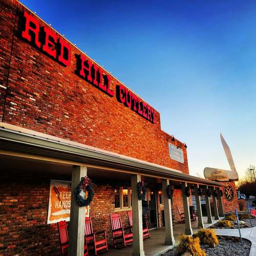Exterior of Red Hill Cutlery building at sunset, featuring brick facade, red rocking chairs, and a large knife sign.