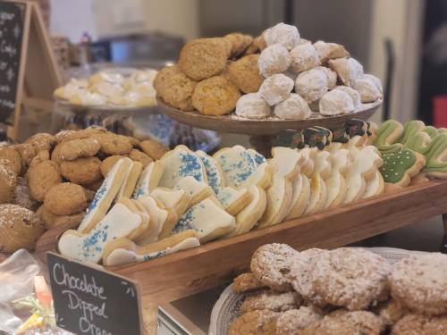 A variety of decorated cookies and treats displayed on wooden trays, including chocolate-dipped and powdered sugar cookies.