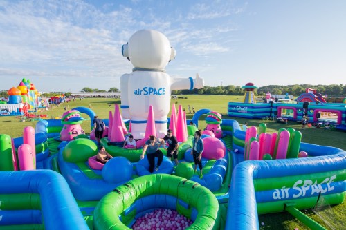 A colorful inflatable playground with a large robot figure, featuring slides and play areas, set in a sunny outdoor field.