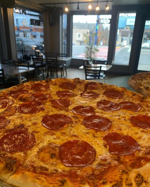 A close-up of a pepperoni pizza on a table, with a cozy restaurant interior and large windows in the background.