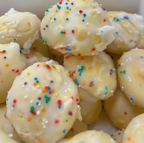 A close-up of white frosted cookies topped with colorful sprinkles, piled in a white container.