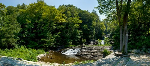 A serene landscape featuring a flowing river surrounded by lush green trees and rocky terrain under a clear blue sky.