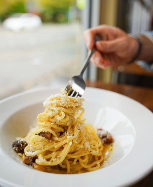 A fork twirls spaghetti topped with grated cheese in a white bowl on a wooden table.