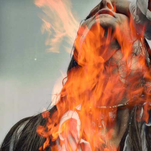 A person with long hair tilts their head back, surrounded by flames, creating a dramatic and intense visual effect.